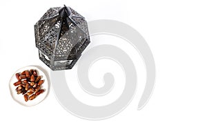 Ornamental dark Moroccan, Arabic lantern and plate with date fruits on white table. Greeting card for Muslim holy month
