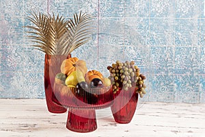 Ornamental pumpkin, fruit and grapes in a vase. Colored Glass vase fruit holder. Red glass decanter with its lid removed