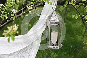 Ornamental silver Moroccan lantern handing on blooming tree. Green blurred background with white veil. Greeting card