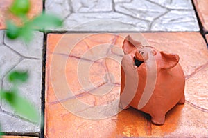 Ornamental terracotta garden doll in the shape of little adorable pig smiling happily on stone tile pavement floor in home garden