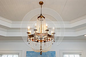 An ornate beaded chandelier light fixture with glowing lit candle type bulbs against a double tray white ceiling