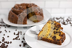 An ornate and decorative homemade and fresh chocolate chip bundt cake with a clice cut out on top of a serving plate