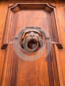 An ornate wood carved door handle and knocker. Lion head shaped.