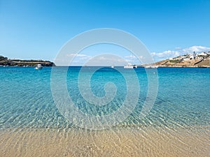 Ornos empty sandy beach, calm sea moored yachts background. Mykonos island, Cyclades Greece