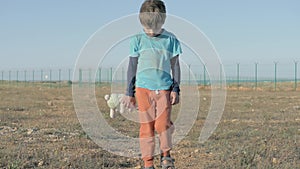 Orphan. Abandoned lonely child on area of the refugee camp. boy in dirty threadbare clothes holding toy plush bunny homeless littl