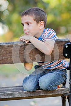 Orphan, unhappy boy sitting on a park bench and crying