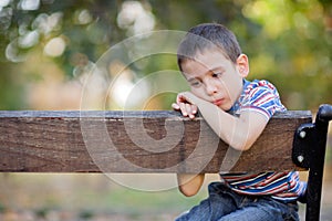 Orphan, unhappy boy sitting on a park bench and crying