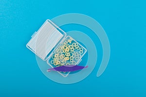 Orthodontic Elastic bands for braces, correcting an overbite. Hook for putting on braces and Ortho wax in plastic box on blue photo