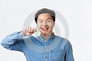 Orthodontics, dental care and hygiene concept. Close-up of friendly-looking smiling asian man brushing teeth with braces