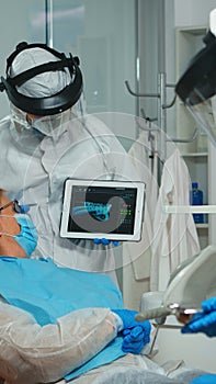 Orthodontist in coverall using tablet explaining dental x ray