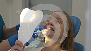 Orthodontist puts rubber rods on patient's braces. Woman holds mirror in front of her face and looks at what doctor is