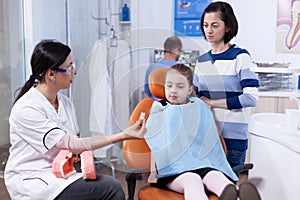 Orthodontist showing kid and her mother sample of teeth
