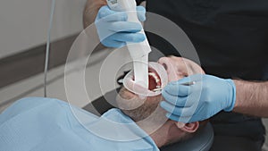 Orthodontist using 3D intraoral scanner for scanning teeth patient's. The dentist holds in his hand a manual 3D