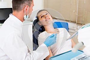 Orthodontist in white is taking a view of an adult woman on the chair