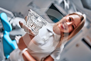 Orthodontology and prosthetics concept. Female dentist wearing white gloves holding plastic jaw model