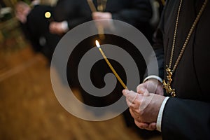 Orthodox Christian priest praying in the church with burning candle in hands.