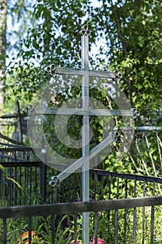 Orthodox iron cross on a grave in a Christian cemetery in summer vegetation. Memory and sorrow. Vertical