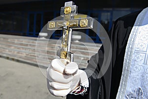 Orthodox Priest in protective gloves as a preventive measure against the coronavirus COVID - 19 holds the crucifixion