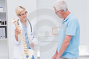 Orthopedic doctor explaining anatomical spine to senior man