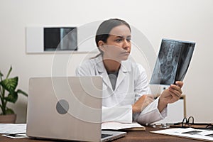 orthopedic doctor reviews patient X-ray films scans while working with laptop, online medicine.