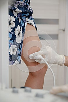 An orthopedic surgeon performs an ultrasound examination of the patient`s leg veins in his office