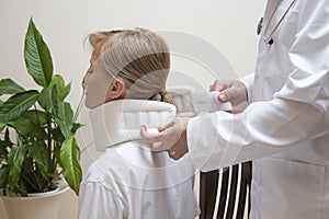 Orthopedic surgeon puts on a white orthopedic collar of a young woman sitting on a chair.