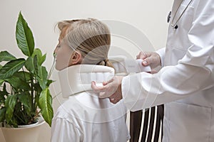 Orthopedic surgeon puts on a white orthopedic collar of a young woman sitting on a chair. photo