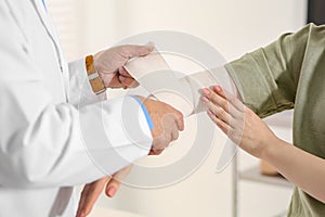Orthopedist applying bandage onto patient`s elbow in clinic, closeup
