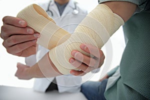 Orthopedist applying bandage onto patient`s hand in clinic