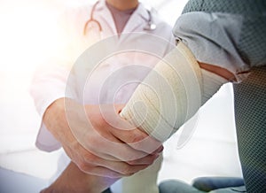 Orthopedist applying bandage onto patient`s hand in clinic