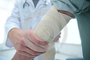 Orthopedist applying bandage onto patient`s hand in clinic