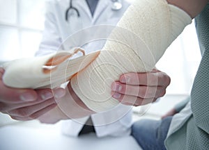 Orthopedist applying bandage onto patient`s hand in clinic photo