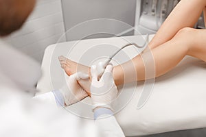 Orthopedist doctor doing ultrasound examination of patient`s foot joints in his office. Young woman passing ultrasound