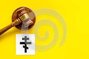 Ortodox cross - Christianity symbol - near gavel on yellow background top-down. Religious conflict concept. Copy space