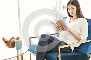 Ortrait Asian woman reading book and relaxing with coffee at home