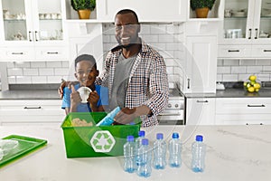 ortrait of happy african american father and son in kitchen sorting rubbish for recycling