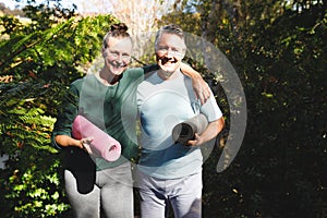 ortrait of happy senior caucasian couple holding yoga mats, looking to camera in sunny garden