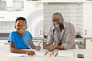 ortrait of smiling african american father and his son in kitchen, doing homework together