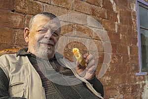 ortrait of smiling Ukrainian senior man while standing against brick wall and holding handmade patty