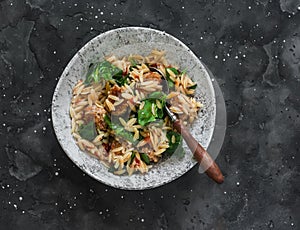 Orzo pasta with meatballs and spinach in tomato sauce on a dark background, top view