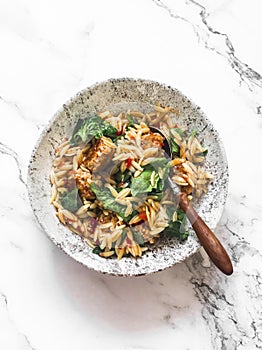 Orzo pasta with meatballs and spinach in tomato sauce on a marble background, top view