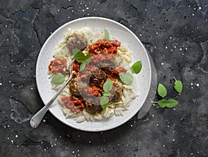 Orzo pasta with meatballs and tomato sauce on dark background, top view
