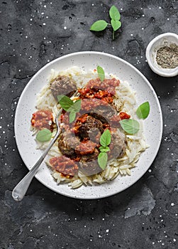 Orzo pasta with meatballs and tomato sauce on dark background, top view