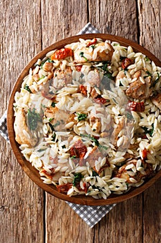 Orzo pasta salad with grilled chicken, sun-dried tomatoes, spinach, garlic and cheese close-up on a plate. Vertical top view