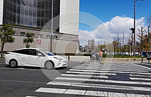 Osaka, Japan on April 10, 2019. Situation at a pedestrian crossing, where a white sporty car stops when a couple riding a bicycle