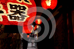 Closeup Black Japanese texts on red paper lantern hanging under Japanese restaurant eaves