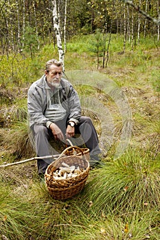 Oscow region, Russia - September, 03, 2011: An elderly man sits in the forest with a basket of mushrooms.