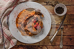 Ossobuco in cooking sauce with carrot, onion, bell pepper and mushrooms accompanied with sweet potato puree in a white platte in