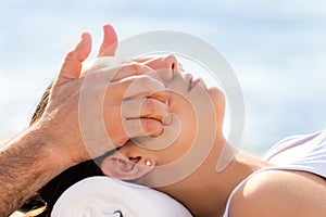 Osteopath doing treatment on female cheek outdoors.