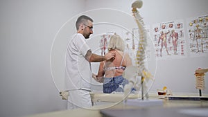 Osteopath examines a senior woman's spinal in a medical center. Posture correction and back pain treatment.